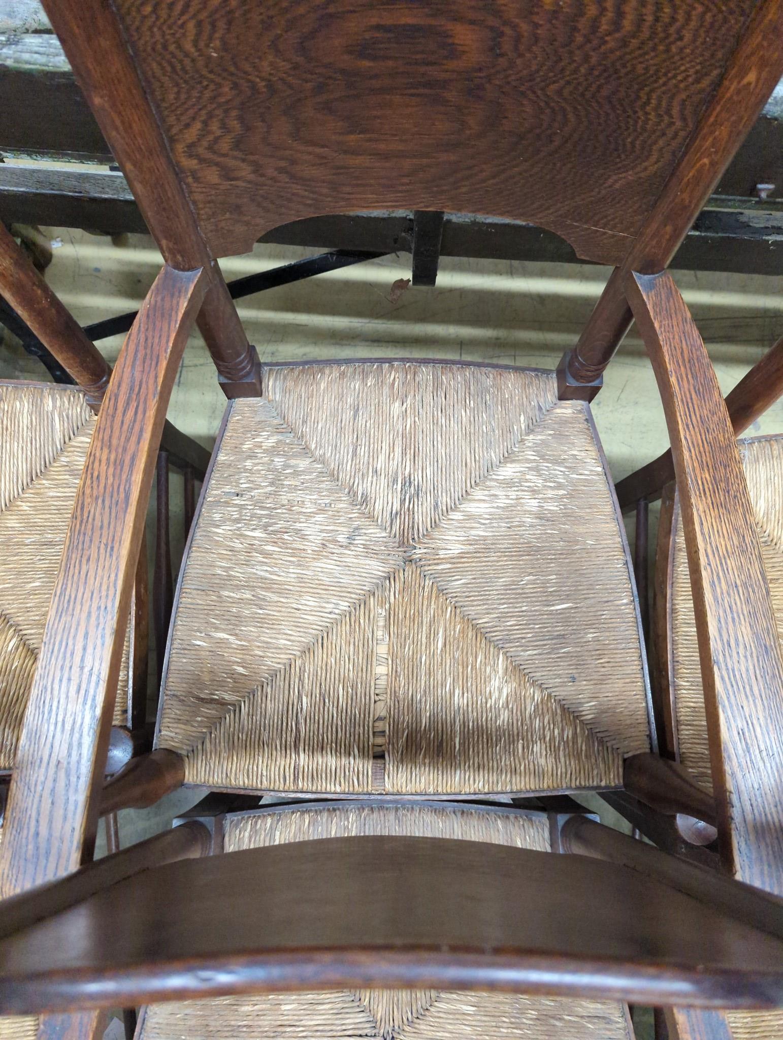 A set of six Arts & Crafts oak chairs, including a pair of carvers, in the Glasgow School manner by William Birch, High Wycombe, with shaped panels backs, ring turned frames and rush seats, carvers W.58cm D.54cm H.109cm